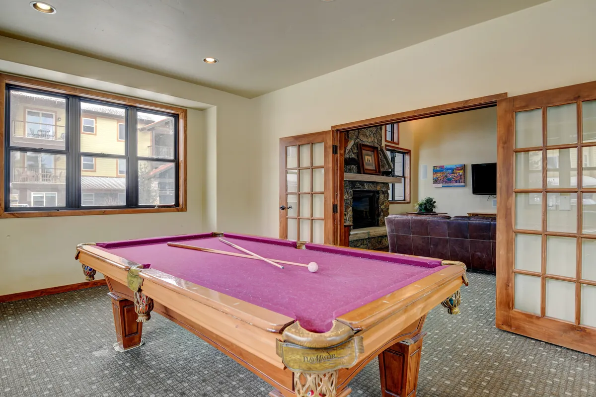 A stylish game room featuring a pool table, large windows with plenty of natural light, and French doors that open to the outside. The space invites guests to enjoy friendly competition and social hangouts in a relaxed setting.