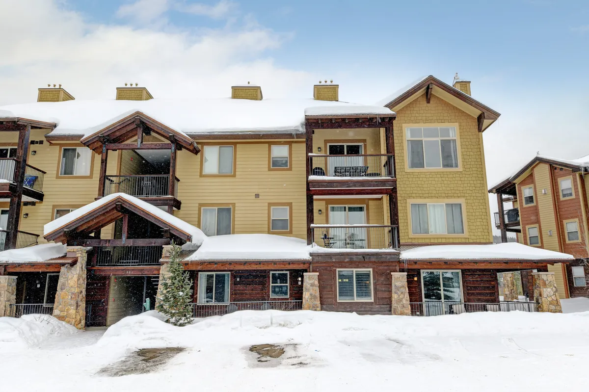 A tranquil exterior view of the resort showcases wooden balconies, stone accents, and a snow-covered roof, highlighting the property's cozy, mountain-lodge feel. The wintry setting conjures images of adventurous days and relaxing evenings spent in comfort.