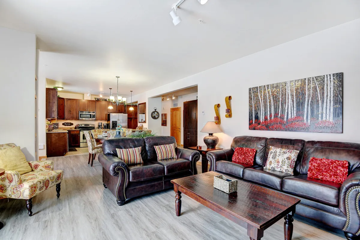 A welcoming interior living area with leather sofas, a coffee table, decorative wall art, and a visible kitchen area. The mood is social and inviting, suggesting a space ideal for family gatherings and game nights.