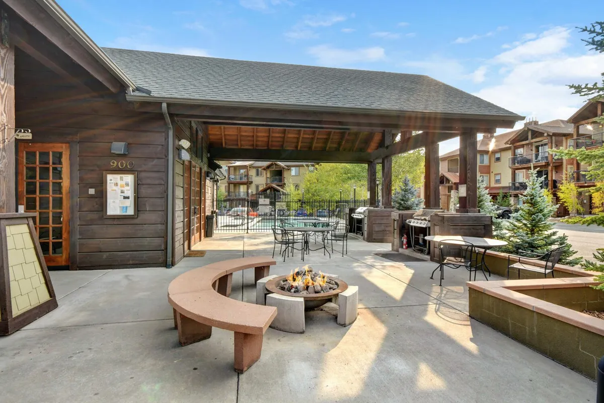 An exterior scene featuring a stylish outdoor fire pit area surrounded by comfortable seating, a barbecue area, and attractive landscaping. The communal atmosphere is designed for social gatherings, relaxation, and enjoying evenings outdoors.