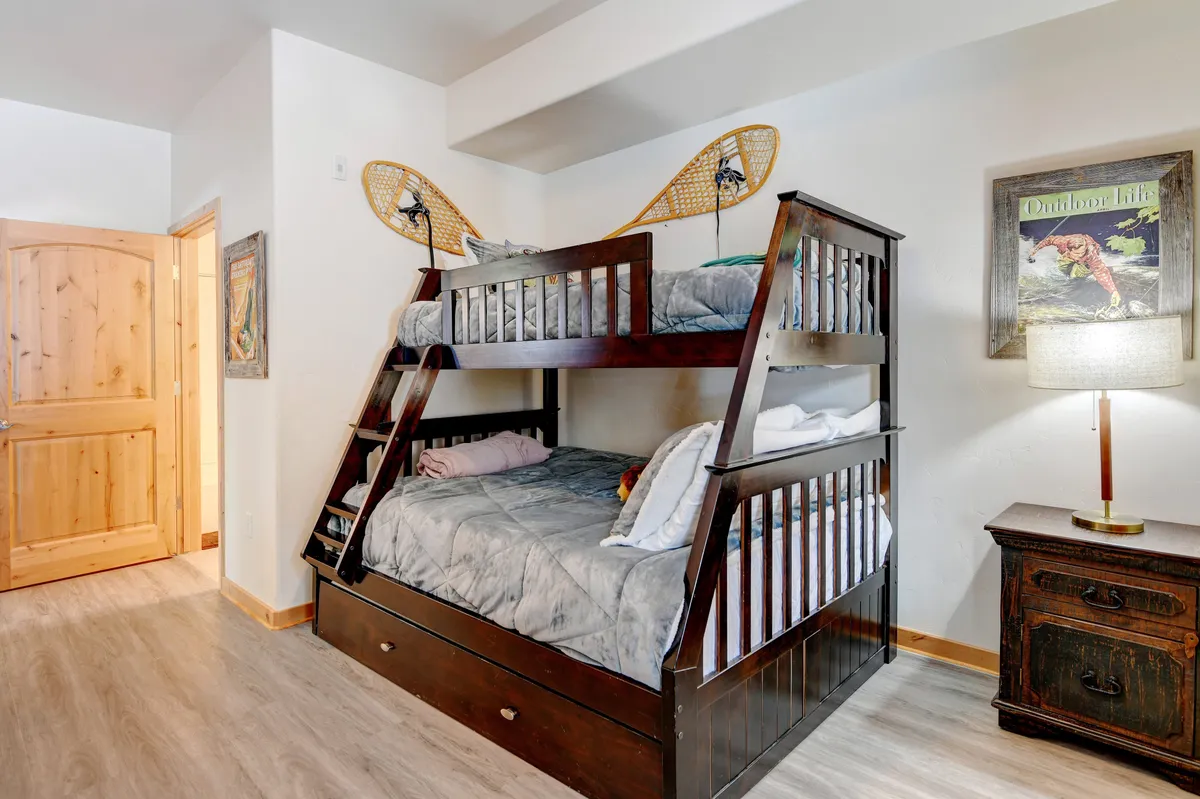 A cozy bunk room with a sturdy bunk bed, decorative snowshoes mounted on the wall, and a nightstand with a lamp. The playful yet restful ambiance makes it suitable for children or extra guests seeking a fun and comfortable stay.
