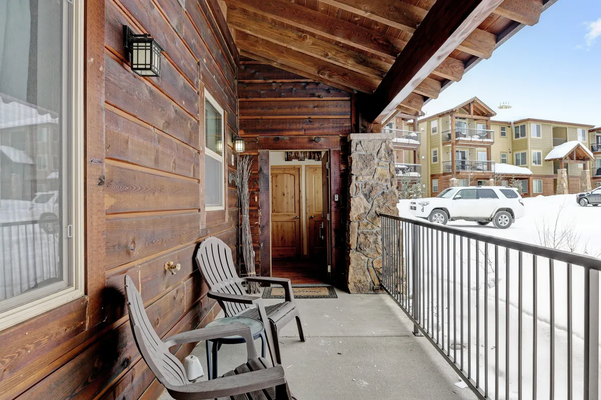 An inviting exterior view of the property with a wooden front door, stone accents, adirondack chairs, and a snow-covered ground. The scene feels cozy and welcoming, suggesting the perfect retreat after a day of adventure. The porch area is pet-friendly, ideal for relaxing with your dog.