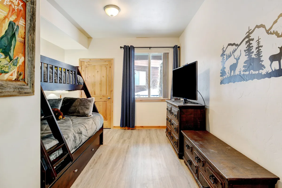 A family-friendly bedroom featuring a bunk bed, TV, and mountain-themed wall art. Sunlight streams in through the window, creating a playful yet restful atmosphere. The space is perfect for flexible sleeping arrangements for families with children or groups.