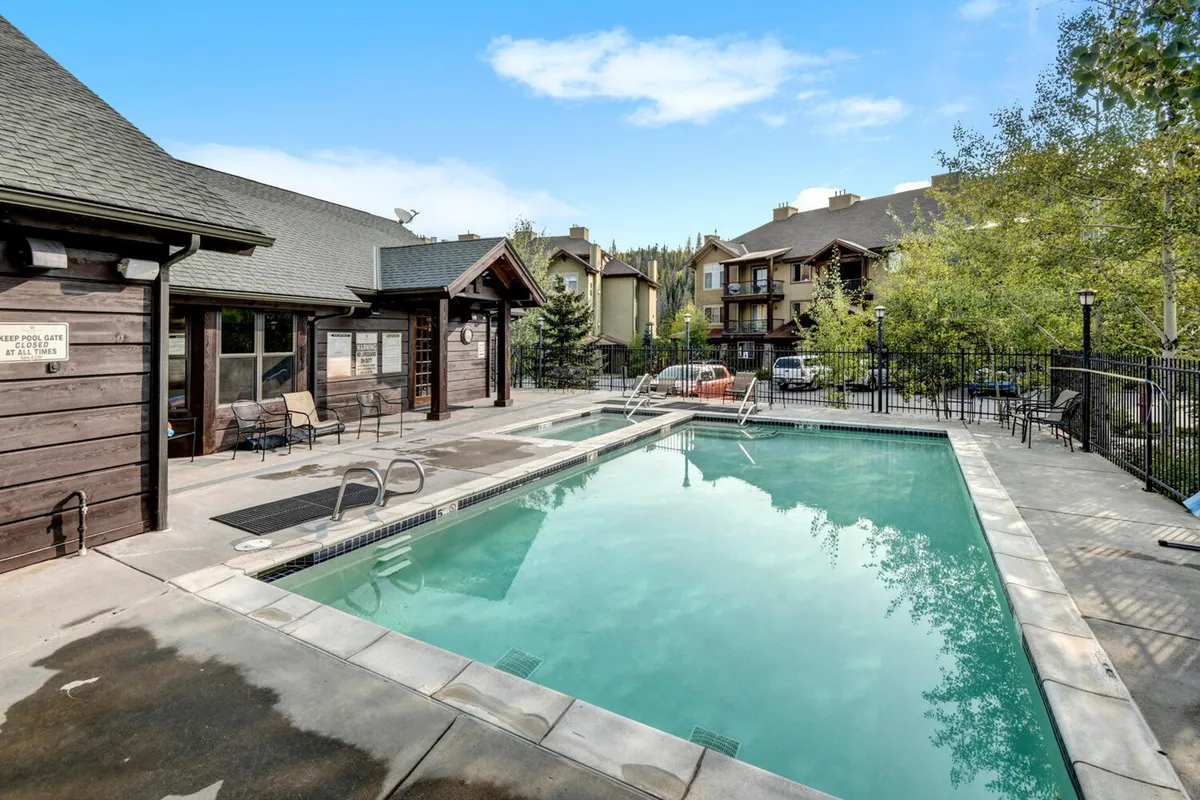 This image showcases a beautiful heated outdoor swimming pool surrounded by lounge chairs and lush trees, with adjacent buildings visible in the background. The space suggests an inviting area for swimming, sunbathing, and poolside relaxation.